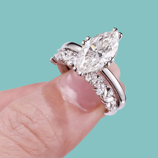 Marquise cut Diamond ring on a finger with wedding band against a teal background