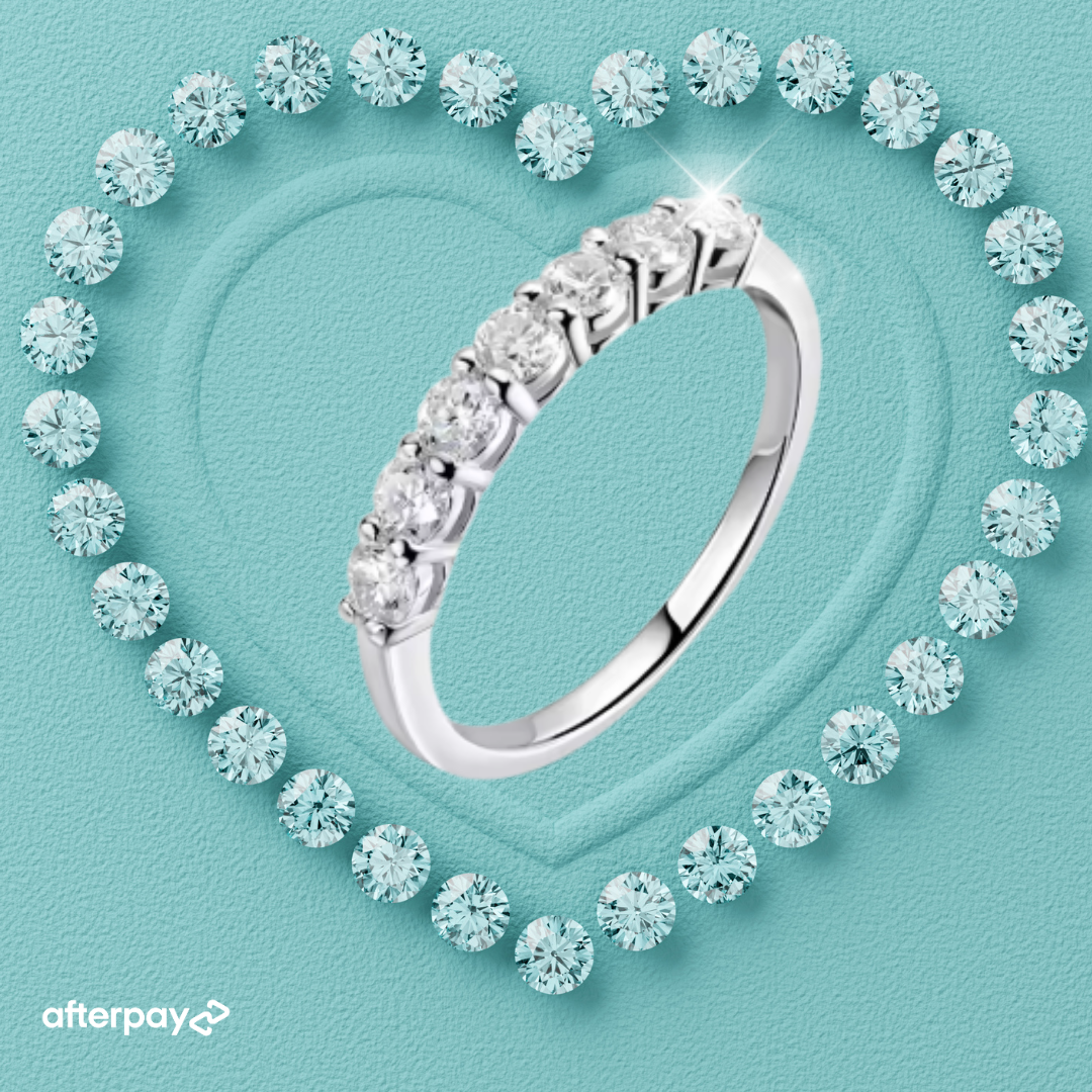 Moissanite wedding band surrounded by smaller diamonds on a light blue background with Afterpay logo.