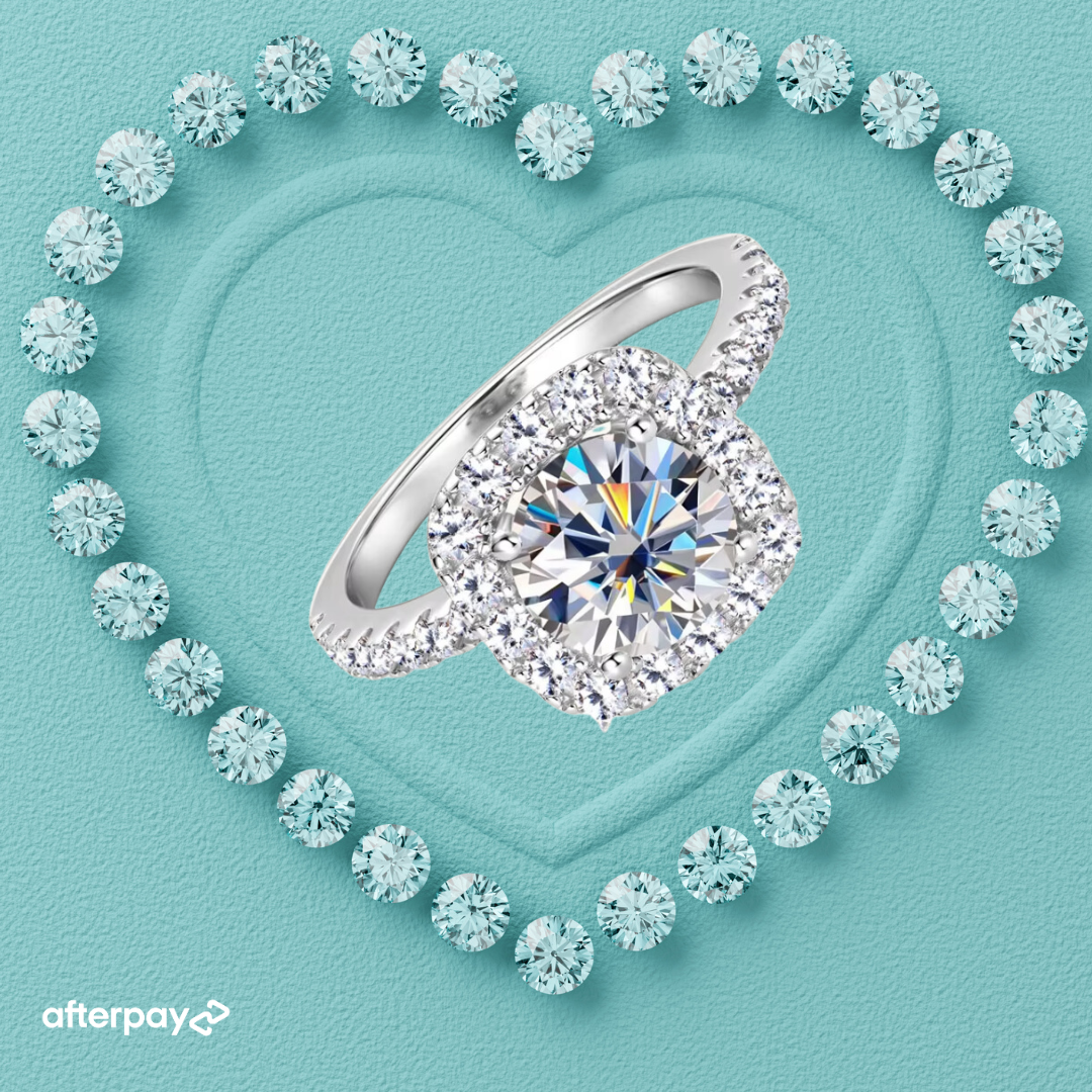 A 2-carat halo moissanite ring with a round brilliant cut, surrounded by smaller sparkling stones, displayed on a heart-shaped setting on a light blue background.