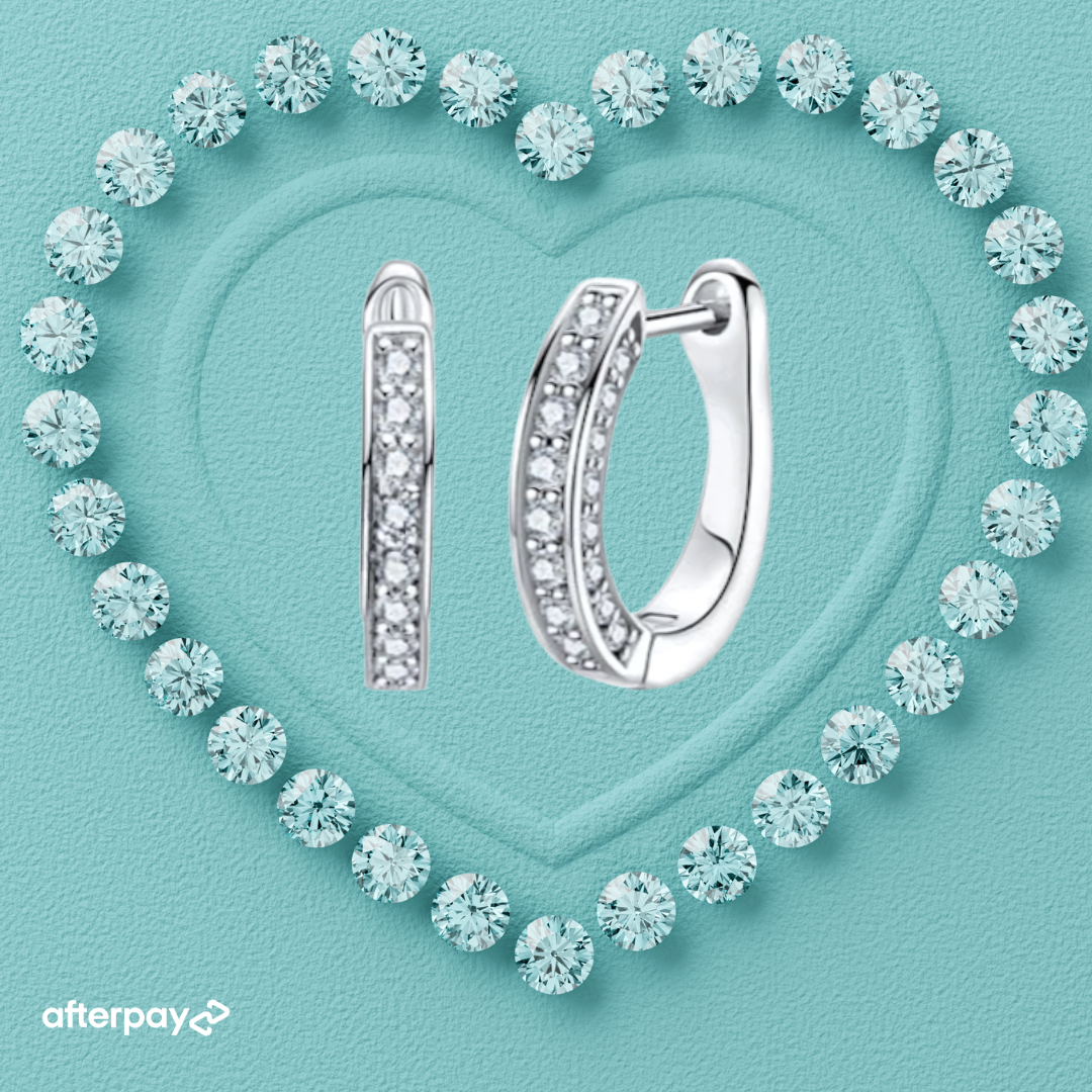 Silver hoop moissanite earrings on a turquoise background with diamond-like crystals forming a heart shape.