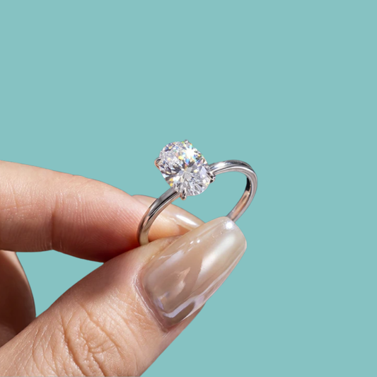 Silver ring with a large diamond held by a hand against a teal background