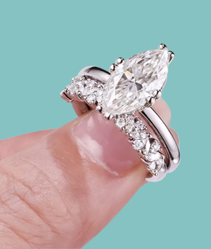 Marquise cut Diamond ring on a finger with wedding band against a teal background