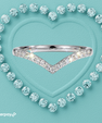 A silver V-shaped ring set with clear pavé stones, centered on a textured light teal background with a heart outline made of round clear stones. An Afterpay logo appears in the bottom-left corner.