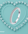 A silver-toned eternity ring set with round brilliant-cut diamonds, presented on a textured light blue background with a heart-shaped border of matching diamonds. The Afterpay logo is visible in the bottom-left corner.