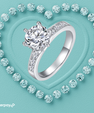 A silver moisasnite 2 carat engagement ring with a large round-cut diamond center stone and smaller diamonds along the band, displayed on a turquoise heart-shaped background surrounded by small diamond-like stones. The Afterpay logo appears in the lower-left corner.
