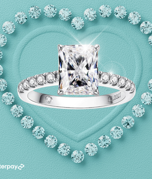 A radiant cut moissanite ring with diamond accents on the band, displayed on a heart-shaped background with diamond patterns.