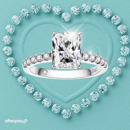 A radiant cut moissanite ring with diamond accents on the band, displayed on a heart-shaped background with diamond patterns.