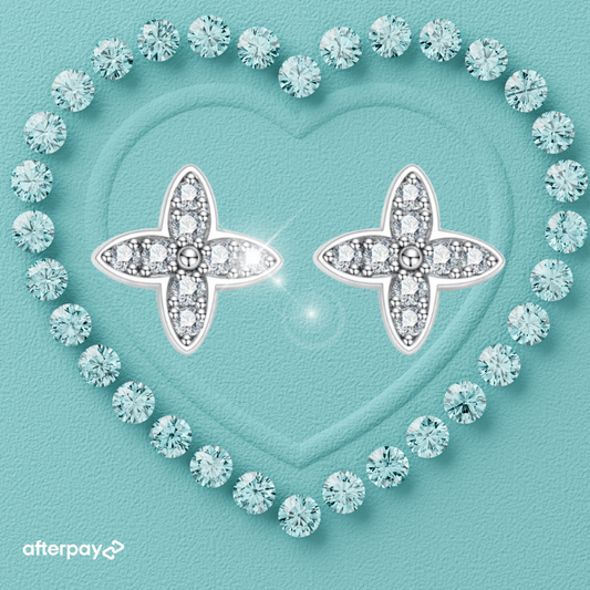 A pair of petal fleur de lis shape moissanite diamond earrings with a heart-shaped design, surrounded by smaller clear crystals, set on a teal background with a textured surface.