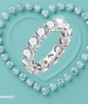 A loop-shaped moissanite eternity ring with round-cut stones set in a heart-shaped arrangement with a bright blue background, showcasing the ring's brilliance and sparkle.