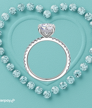 Silver hidden halo round moissanite diamond ring surrounded by smaller diamonds on a light blue background with Afterpay logo.