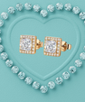 A pair of square yellow gold stud earrings with princess-cut clear center stones and a halo of smaller clear stones, arranged on a turquoise heart-shaped background surrounded by matching clear stones.