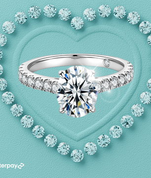 An oval moissanite ring with a 2-carat oval moissanite center stone set in a pavé band, surrounded by smaller moissanite stones on a heart-shaped pattern on a blue background.