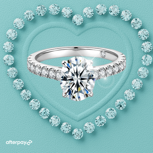 An oval moissanite ring with a 2-carat oval moissanite center stone set in a pavé band, surrounded by smaller moissanite stones on a heart-shaped pattern on a blue background.