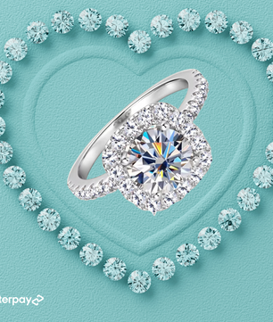 A 2-carat halo moissanite ring with a round brilliant cut, surrounded by smaller sparkling stones, displayed on a heart-shaped setting on a light blue background.