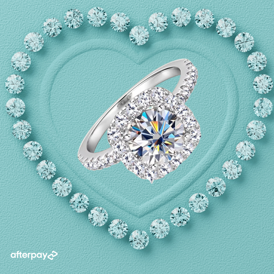 A 2-carat halo moissanite ring with a round brilliant cut, surrounded by smaller sparkling stones, displayed on a heart-shaped setting on a light blue background.