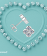 A pair of silver stud earrings arranged on a light aqua textured background, with one earring shown front-facing as a four-petal flower and the other shown side-facing to reveal the post and butterfly back. The earrings are surrounded by a heart-shaped border of clear gemstones, and an Afterpay logo appears in the bottom-left corner.