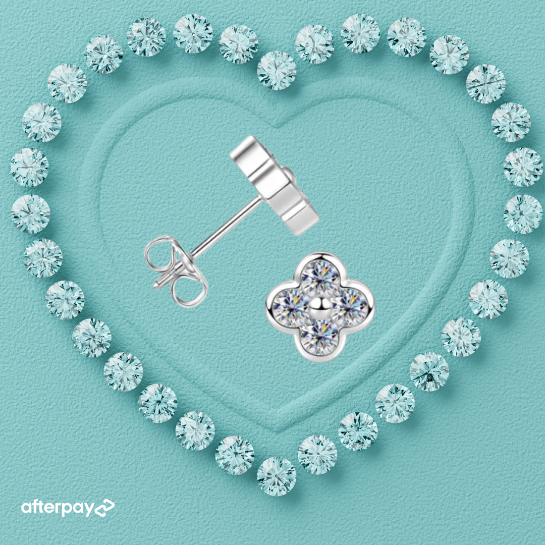 A pair of silver stud earrings arranged on a light aqua textured background, with one earring shown front-facing as a four-petal flower and the other shown side-facing to reveal the post and butterfly back. The earrings are surrounded by a heart-shaped border of clear gemstones, and an Afterpay logo appears in the bottom-left corner.