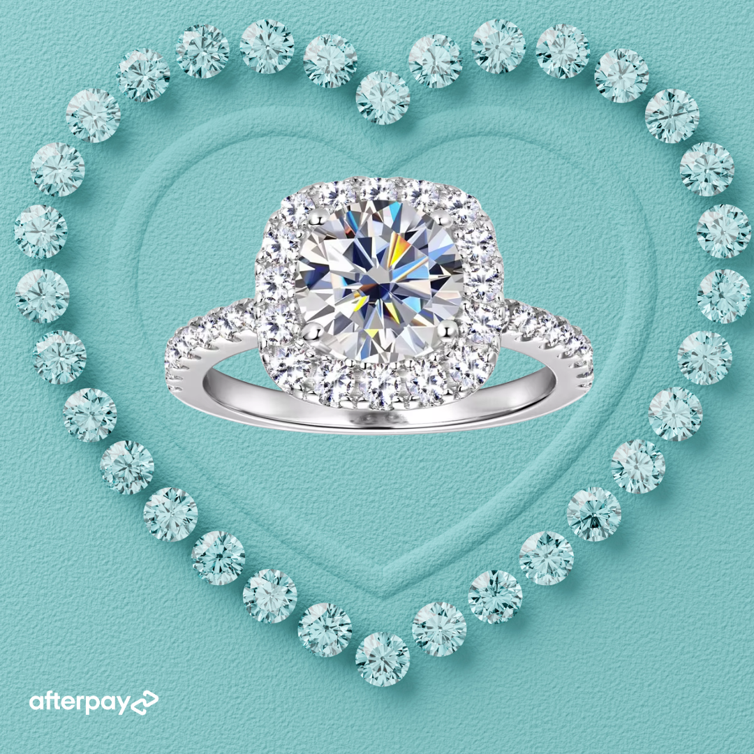 A double-halo diamond engagement ring with a silver-colored band, centered on a textured light blue background with a heart outline made of smaller diamonds. An Afterpay logo is visible in the bottom-left corner.