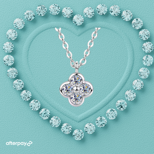 A silver-toned necklace with a four-petal flower pendant set with clear gemstones, centered on a textured aqua background with a heart outline made of matching round clear stones. An afterpay logo appears in the lower-left corner.