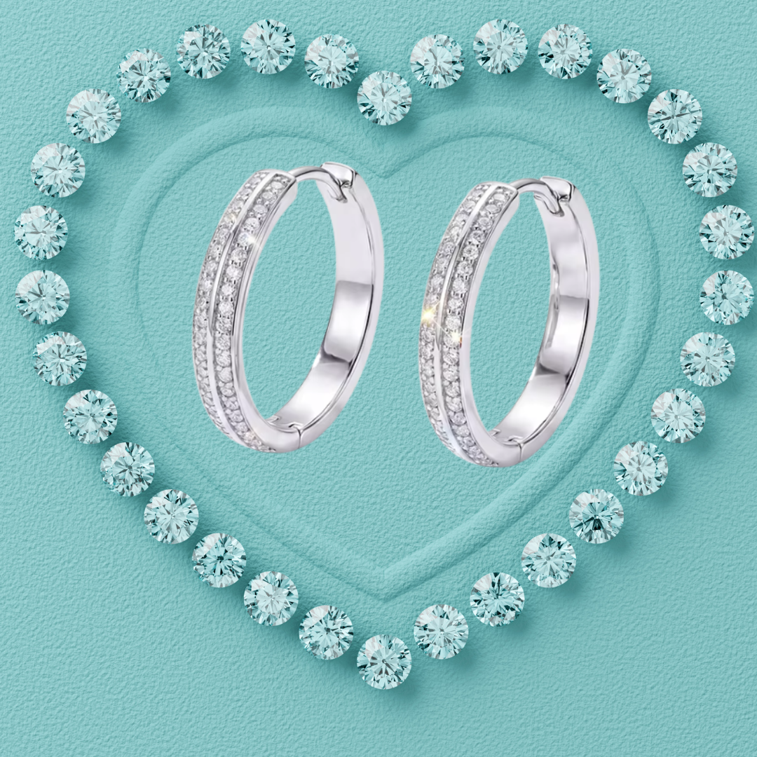 A pair of silver hoop earrings with pavé-set clear stones, arranged on a textured light aqua background with a heart outline made of matching round stones.