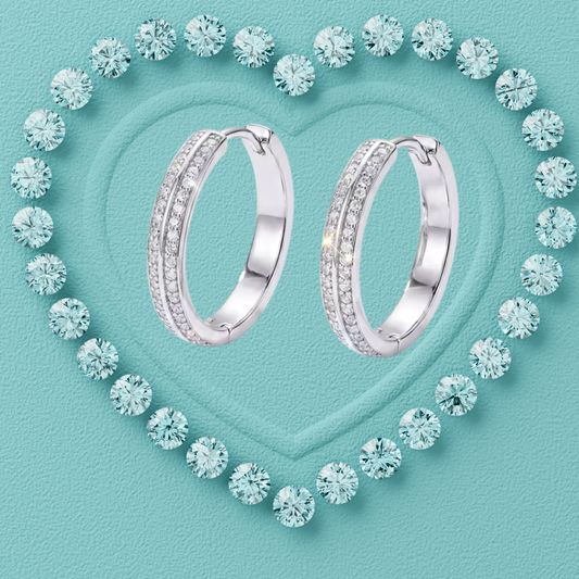 A pair of silver hoop earrings with pavé-set clear stones, arranged on a textured light aqua background with a heart outline made of matching round stones.