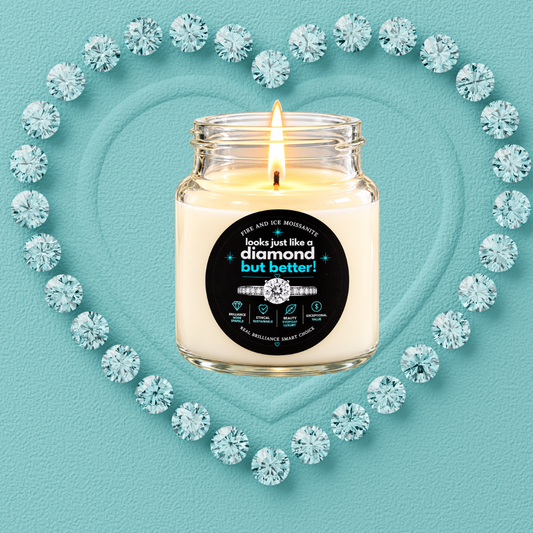 A lit candle in a clear glass jar with a cream wax fill and a black circular label, centered on a turquoise textured background. The label reads 'looks just like a diamond but better!' with a ring graphic.