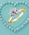 A gold solitaire ring with a round brilliant-cut diamond is centered on a textured light blue background, surrounded by a heart-shaped border of smaller diamonds.