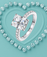 A silver-toned ring with a large square-cut clear center stone and smaller stones along the band, centered on a turquoise heart-shaped background surrounded by small matching stones.