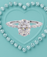 A silver engagement ring with a large oval center stone and marquise-cut side stones, centered on a turquoise heart-shaped background surrounded by small matching stones.