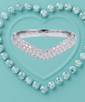 A silver V-shaped diamond ring centered inside a heart outline made of round light blue gemstones on a textured turquoise background.