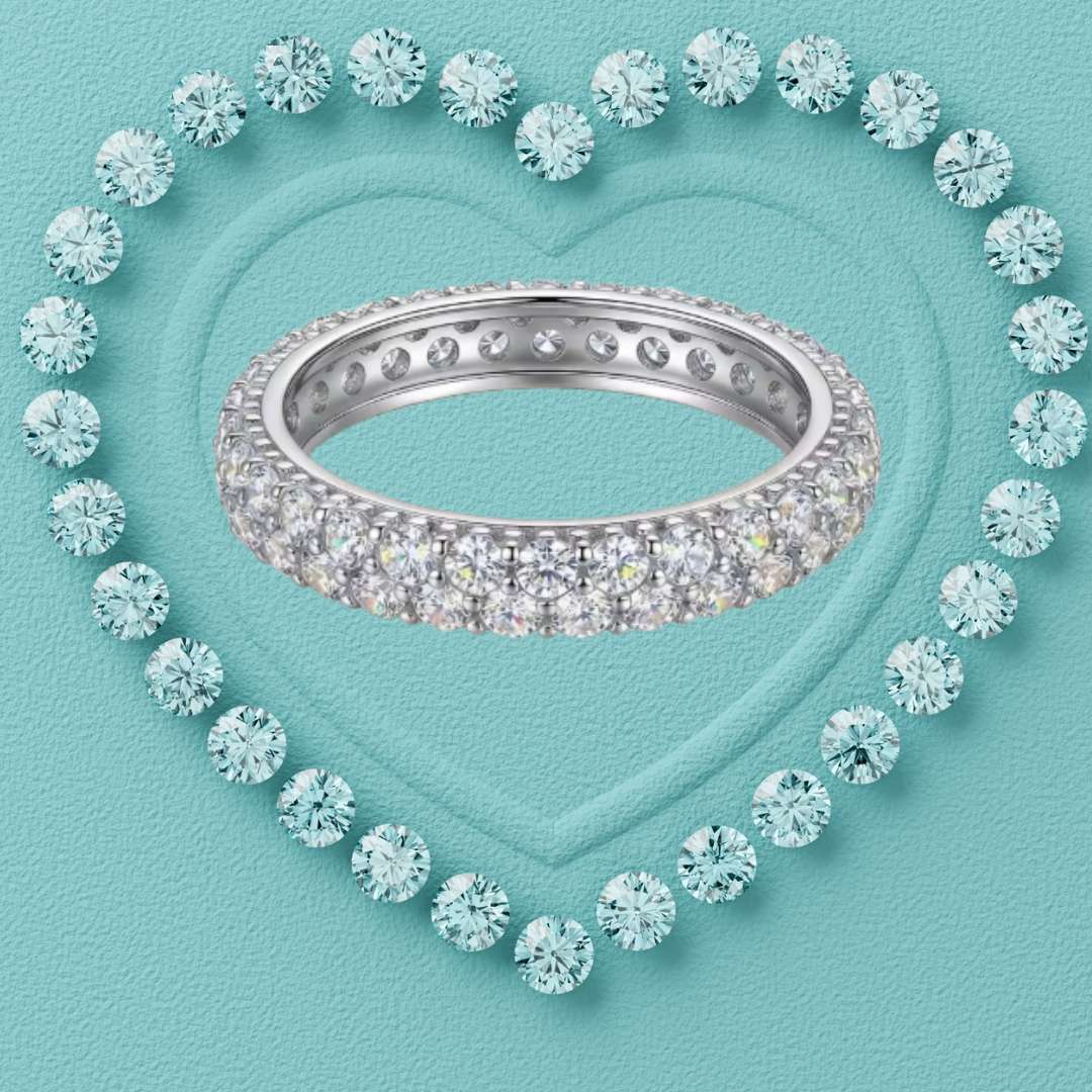 A silver eternity ring paved with clear round-cut gemstones, centered on a textured light blue background with a heart-shaped outline of matching stones.