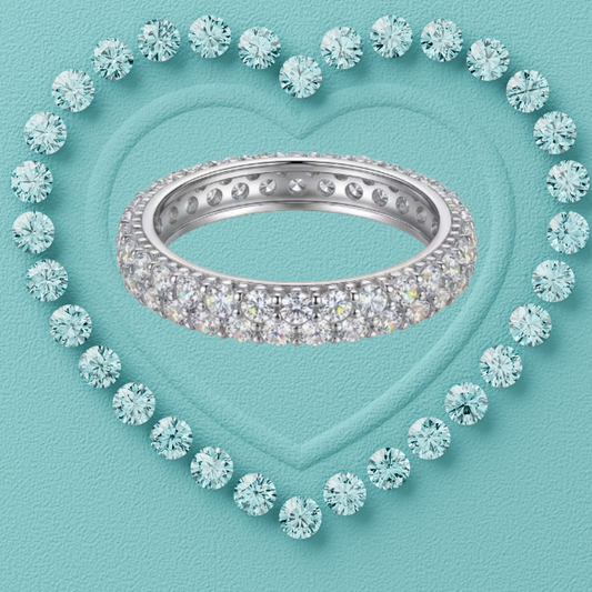 A silver eternity ring paved with clear round-cut gemstones, centered on a textured light blue background with a heart-shaped outline of matching stones.