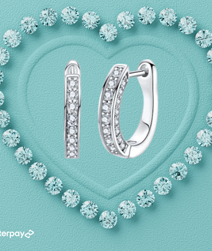 Silver hoop moissanite earrings on a turquoise background with diamond-like crystals forming a heart shape.