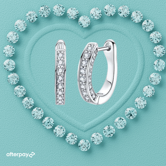 Silver hoop moissanite earrings on a turquoise background with diamond-like crystals forming a heart shape.