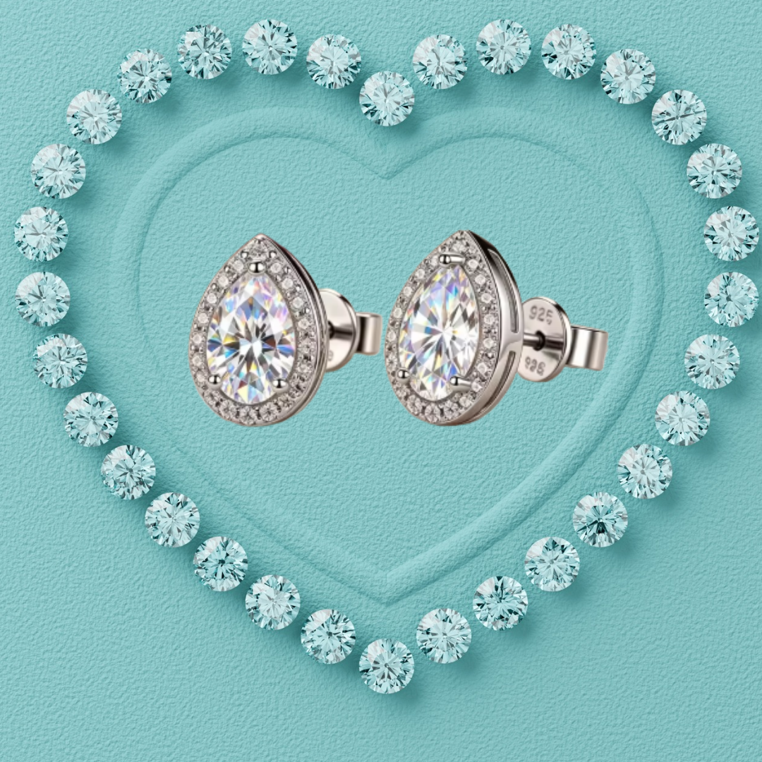 Pear-shaped diamond stud earrings in a silver-toned setting, surrounded by a heart-shaped border of round clear stones on a textured light blue background.