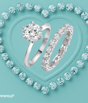 An engagement ring set with a central moissanite stone in a prong setting, accompanied by a matching eternity band, both with multiple surrounding stones on a blue background.