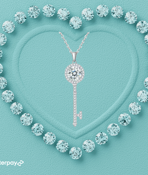 A heart-shaped arrangement of small round diamonds surrounding a prominent round brilliant cut moissanite stone in the center, with a key-shaped pendant also featuring a moissanite stone, displayed on a blue background.