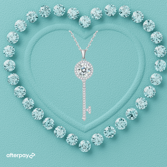 A heart-shaped arrangement of small round diamonds surrounding a prominent round brilliant cut moissanite stone in the center, with a key-shaped pendant also featuring a moissanite stone, displayed on a blue background.