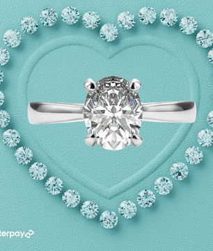 An oval-shaped moissanite stone set in a silver ring, surrounded by smaller round stones on a heart-shaped background.
