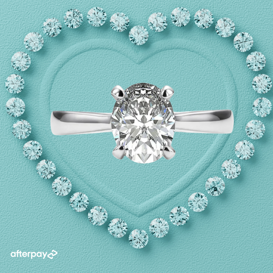 An oval-shaped moissanite stone set in a silver ring, surrounded by smaller round stones on a heart-shaped background.