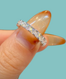 A close-up of a diamond eternity ring on a person's finger, featuring a silver band set with clear round-cut diamonds, set against a solid light teal background.