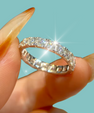 A silver diamond eternity ring held between fingers against a solid light blue background.