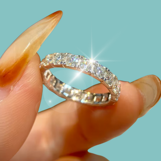 A silver diamond eternity ring held between fingers against a solid light blue background.