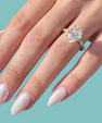 A close-up of a hand with long, glossy pale pink manicured nails wearing a gold solitaire engagement ring with a large clear round gemstone, set against a solid light teal background.