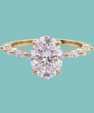 A yellow gold ring featuring a large oval-cut clear center stone and smaller marquise-cut side stones, shown on a solid light teal background.