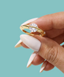 Saturn’s Kiss moissanite ring featuring a round centre stone crossed by a polished gold-toned band, with small side stones.