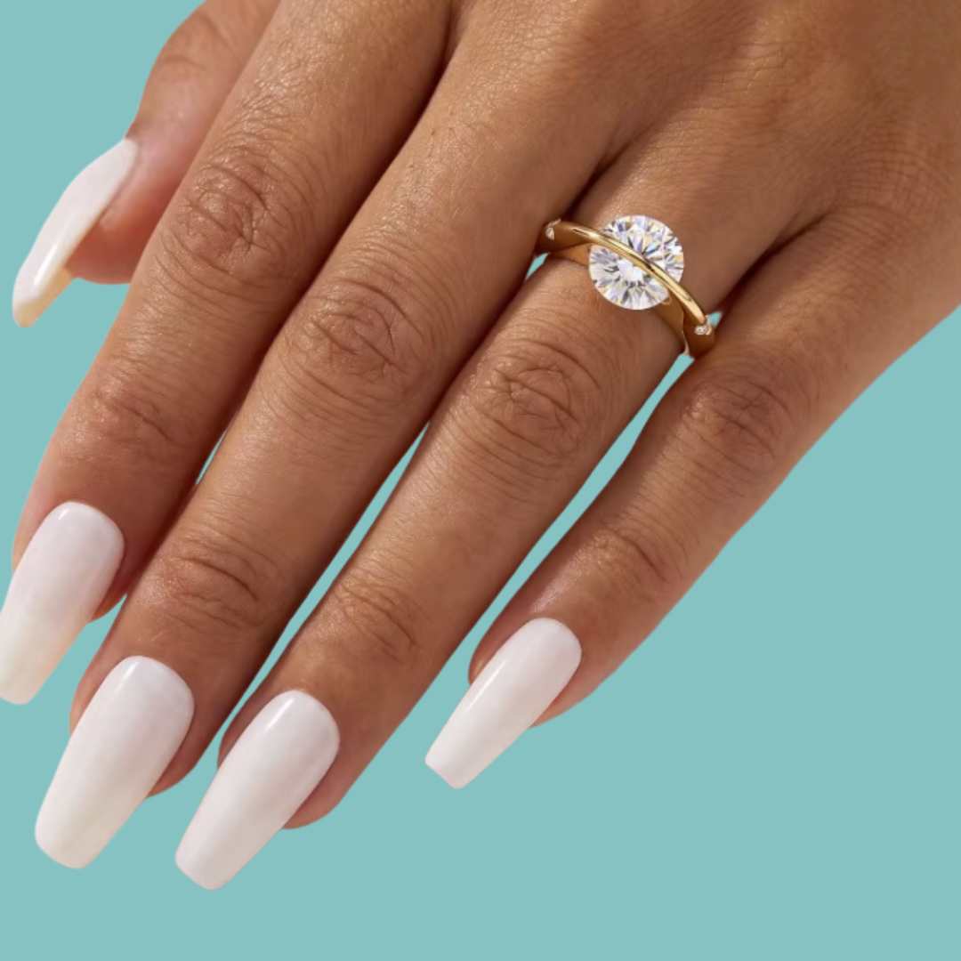 Saturn’s Kiss moissanite ring featuring a round centre stone crossed by a polished gold-toned band on a models hand with small side stones.