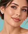Close-up of a woman wearing small teardrop-shaped diamond stud earrings against a solid turquoise background.