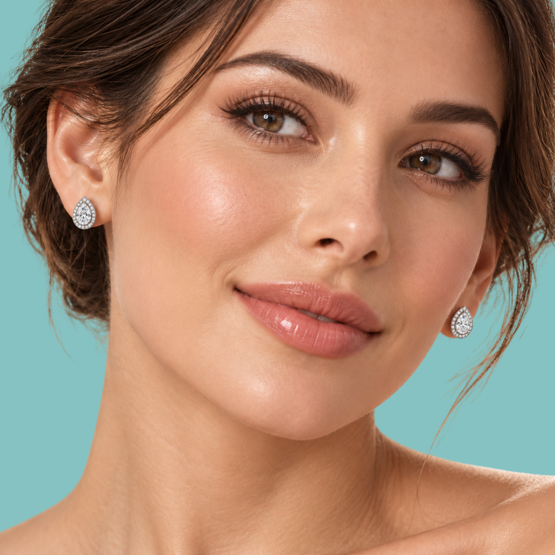Close-up of a woman wearing small teardrop-shaped diamond stud earrings against a solid turquoise background.