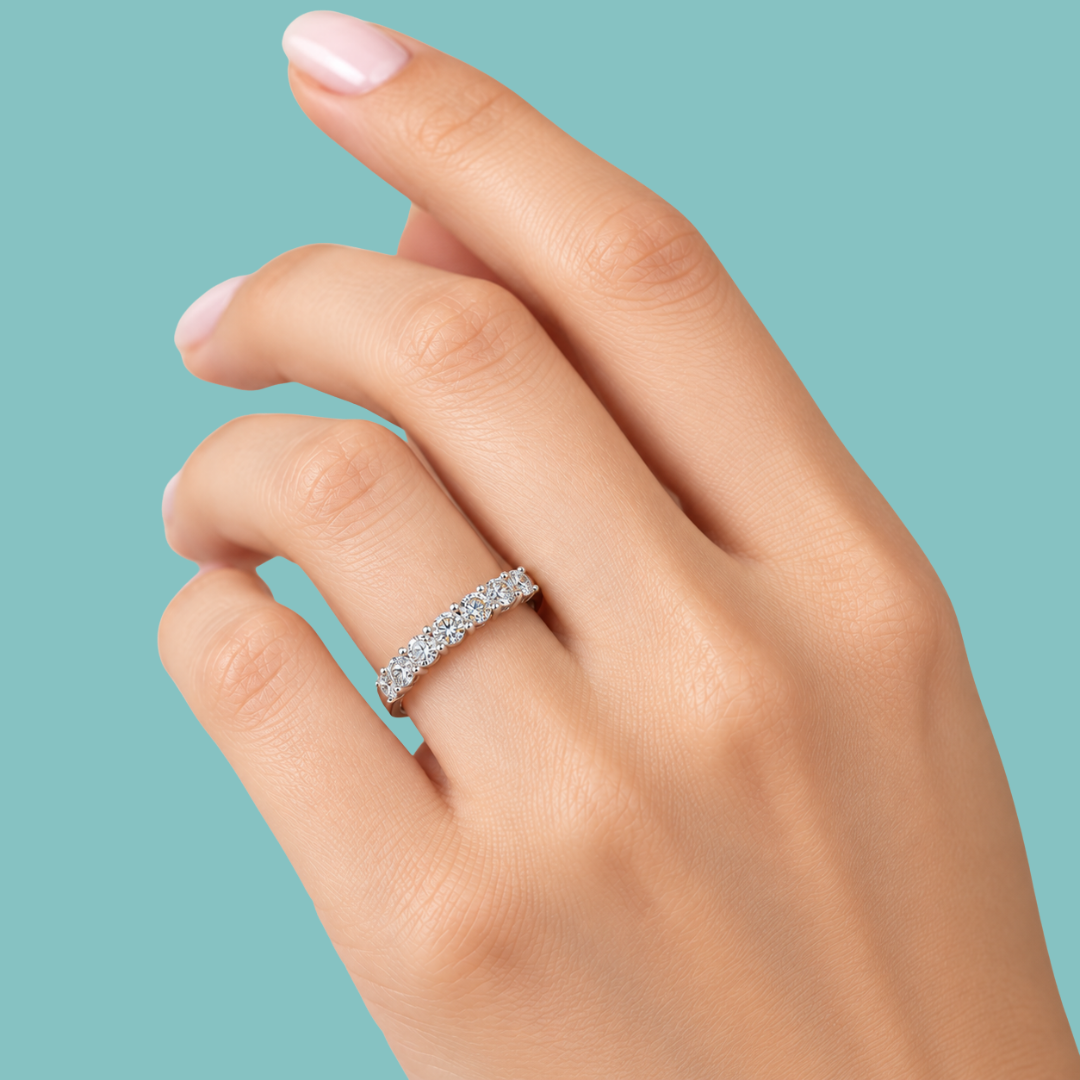 A close-up of a hand wearing a silver diamond eternity ring against a solid teal background.